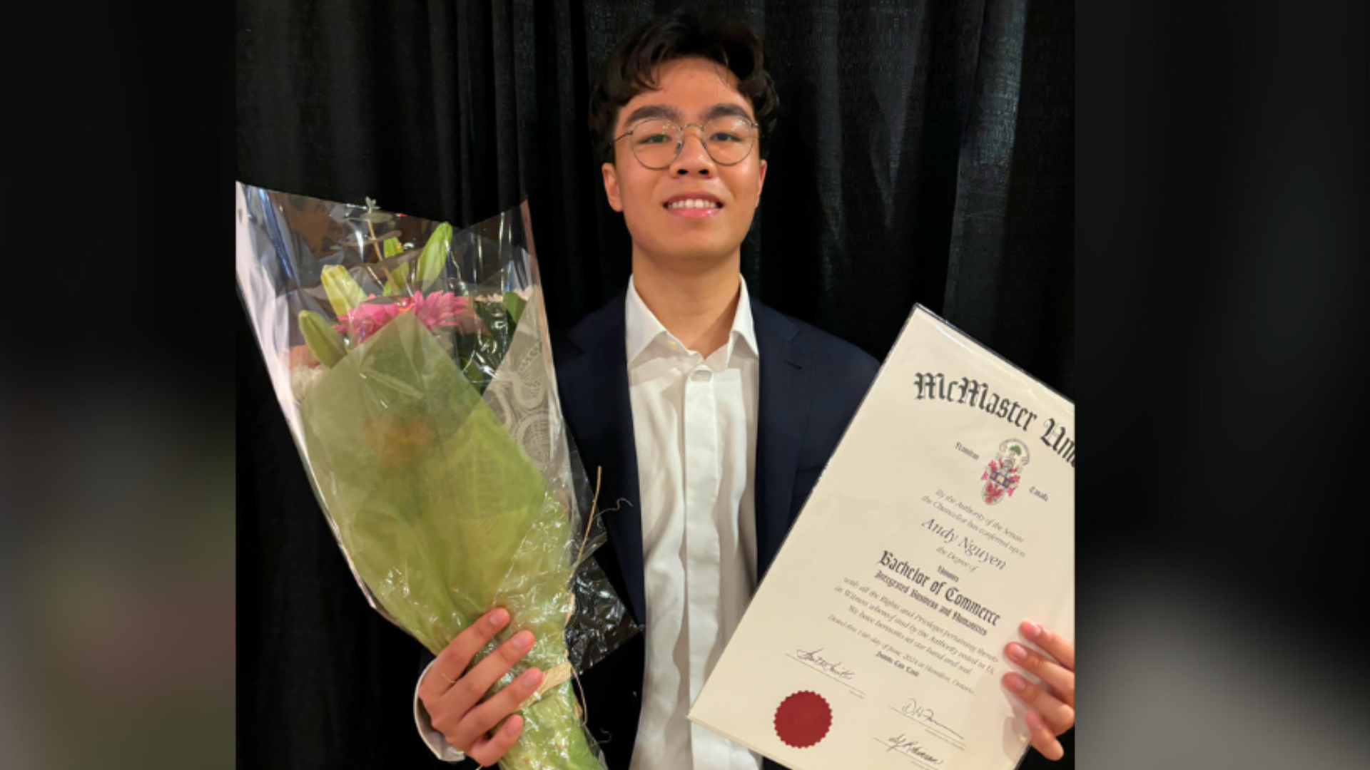 Andy Nguyen, a smiling Asian man wearing glasses and a navy suit, holds up flowers and a bachelor of commerce degree.
