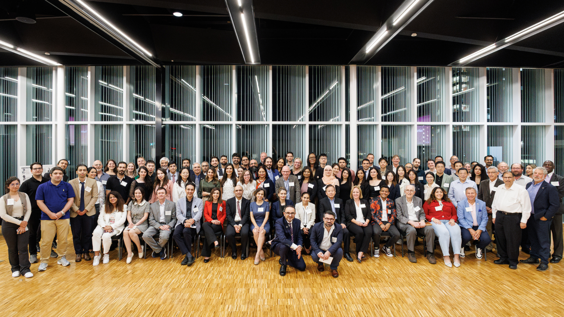 Group photo of about 70 smiling business professionals and PhD students, some seated, some standing in a dining hall.