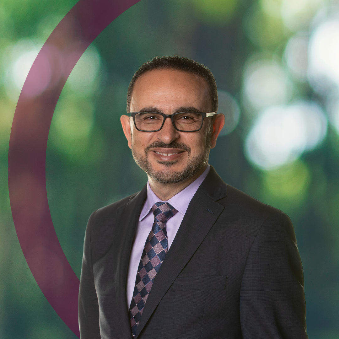 Portrait of Khaled Hassanein, DeGroote Dean, a smiling Arabic man wearing glasses and a dark grey suit and tie.