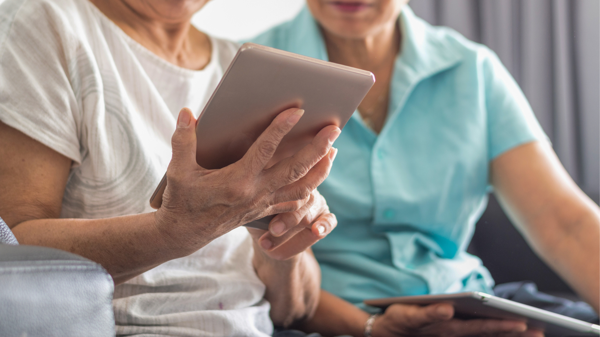 Older person's hands scroll a tablet being shown to a middle-aged person (close-up).
