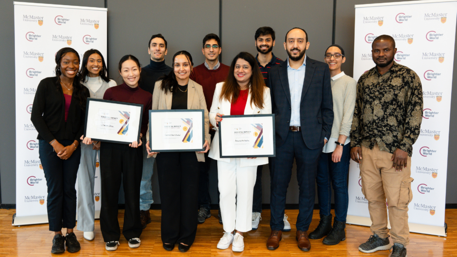 A group of diverse people stand in front of McMaster University banners, holding certificates.