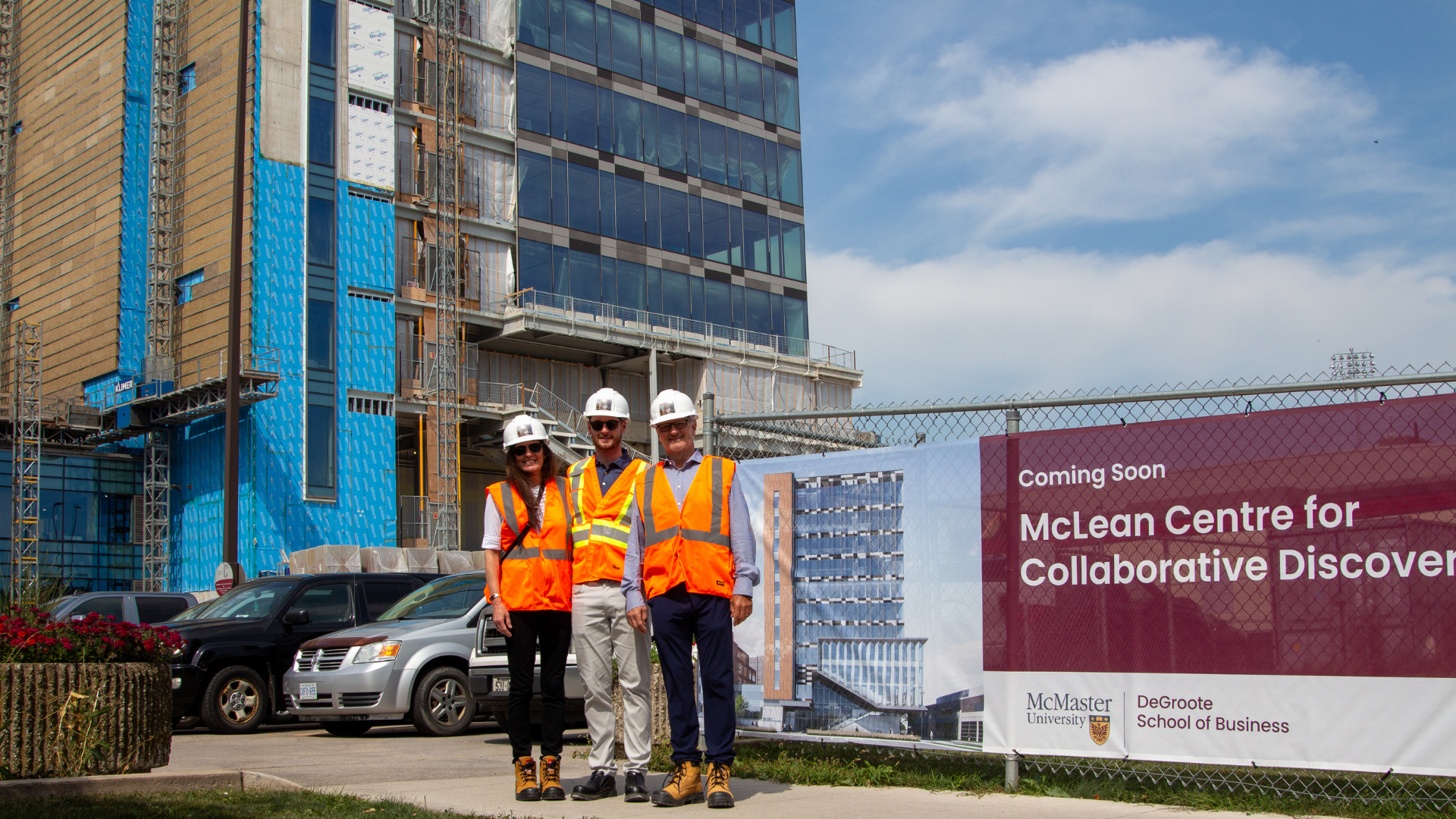 Three professionals wearing white hard hats and safety vests at a construction site.